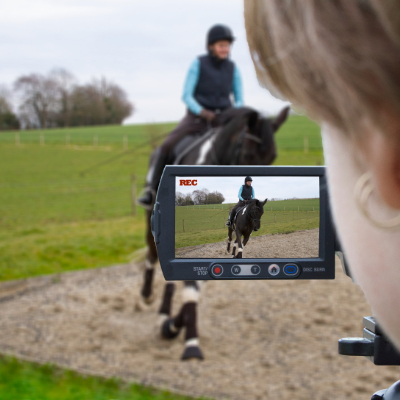 Horse and rider trotting in an arena with a person filming. We can see the rider in the camera filming